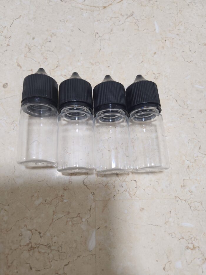 Four empty glass dropper bottles with black caps lined up on a beige marble surface. - Tradedubai.ae Wholesale B2B Market