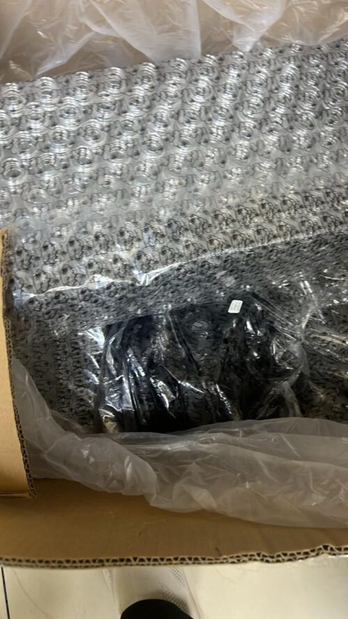 IMG-20260420-WA0005 - Tradedubai.ae Wholesale B2B Market Open cardboard box showing a black item wrapped in clear plastic and bubble wrap with a repeating circular pattern. - Tradedubai.ae Wholesale B2B Market