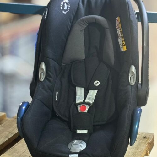 Black Maxi-Cosi infant car seat with five-point harness and buckle, placed on a wooden pallet. - Tradedubai.ae Wholesale B2B Market